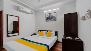 Habitación de hotel con cama, armario, escritorio, espejo, equipo de aire acondicionado y un cuadro en la pared.