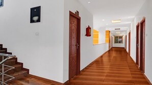 Un pasillo con suelo de madera, paredes blancas y una escalera a la izquierda.