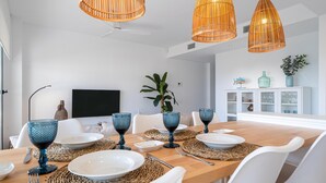 Ein stilvolles Esszimmer mit einem Holztisch, gedeckt für sechs Personen, weißen Stühlen und drei hängenden Korbtreleuchtern.