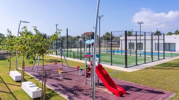 Un parc infantil amb tobogan vermell, cadira de balanceig i una pista de bàsquet.
