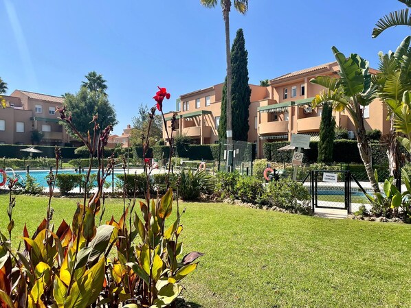 Zona de piscina con un letrero de cerrado, rodeada de césped cuidado y plantas tropicales.
