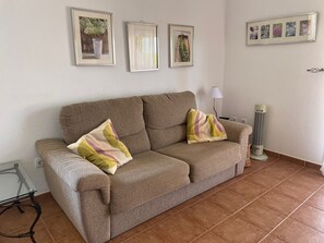 Ein Wohnzimmer mit einem braunen Sofa, zwei Kissen, einem Glastisch, einer Stehlampe und einem Standheizkörper.