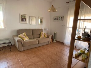 Un salón con un sofá color beige, un calefactor independiente y una ventana con cortinas.