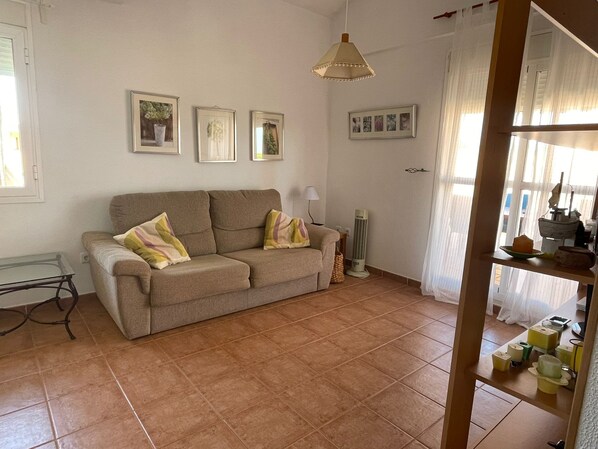 A living room with a beige sofa, a standing heater, and a window with curtains.