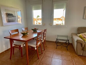 A dining area with a wooden table and chairs, a glass coffee table, and a sofa.