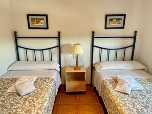 A hotel room with two beds, each with a patterned bedspread and a folded towel. There is a nightstand with a lamp between the beds.