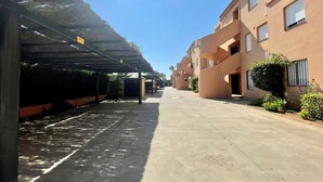 A covered parking area with a clear sky, adjacent to a building with balconies and windows.