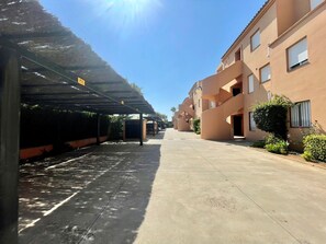 A covered parking area with a clear sky, adjacent to a building with balconies and windows.