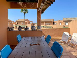 Eine Terrasse mit Holztisch und blauen Stühlen, mit Blick auf eine Reihe von Häusern mit Ziegeldächern.