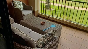 A balcony with wicker furniture, a ceiling fan, and a view of a garden. - Prado Golf Apartment with shared swimming pool (Ayamonte)
