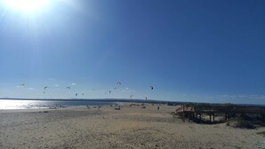 A beach with people, a wooden pier, and kites in the sky. - Prado Golf Apartment with shared swimming pool (Ayamonte)