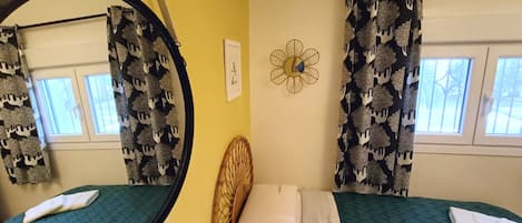 Una habitación con una cama, un espejo redondo, un adorno floral en la pared y una ventana con cortinas.