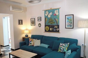 A living room with a teal sofa, a wooden coffee table, and a wall-mounted air conditioner. - Chalet 'El Girasol' near de beach (Chiclana)