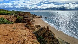 Un paisaje costero con una playa arenosa, acantilados rocosos y cielo despejado.