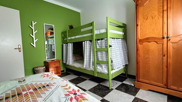 Una habitación con una litera, un armario, un espejo y una colcha estampada.