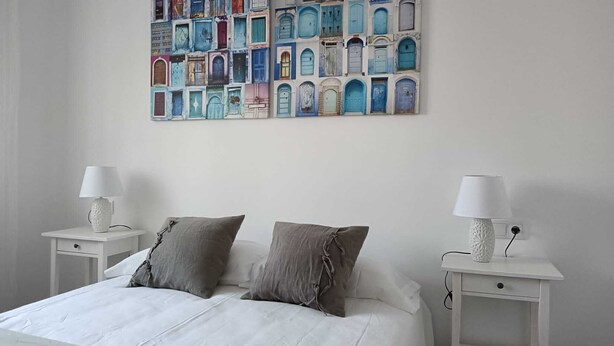 A bedroom with a white bed, two bedside tables with lamps, and a colorful wall art above the bed.