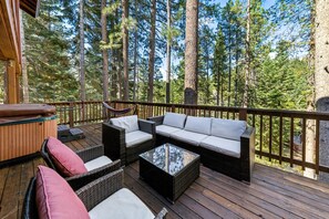 A deck with wicker furniture, a hot tub, and a view of a forest.