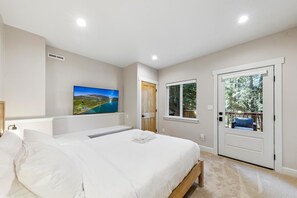 A bedroom with a bed, a TV mounted on the wall, a window, and a door leading to an outdoor area. - 6BR Family Cabin | Sleeps 14 | Hot Tub + Trail (South Lake Tahoe)