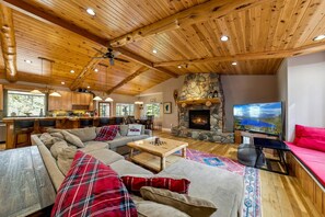 A spacious living area with a stone fireplace, wooden ceiling, and a large TV screen.