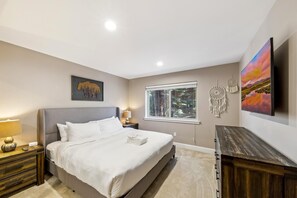 A bedroom with a bed, bedside tables, a window, a wall-mounted TV, and artwork.