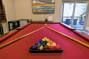 A pool table with a red felt surface, a cue stick, and a rack of billiard balls.