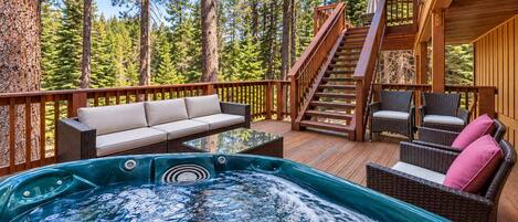 A hot tub on a wooden deck with a staircase, a sofa, and wicker chairs.