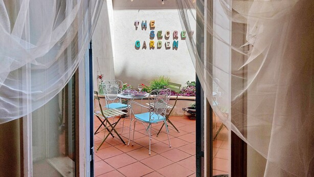 An outdoor patio area with a table and chairs, a wall with the text "THE SECRET GARDEN," and string lights. - LOFT WITH SECRET GARDEN AT THE COLISEUM (roma)