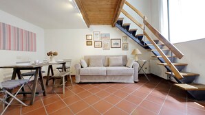 A living room with a wooden staircase, a sofa, a dining table, and artwork on the walls. - LOFT WITH SECRET GARDEN AT THE COLISEUM (roma)