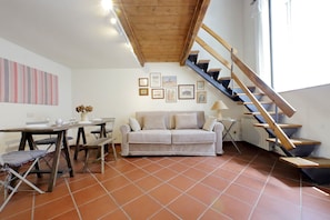A living room with a wooden staircase, a sofa, a dining table, and artwork on the walls.