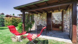 A covered outdoor seating area with two red chairs and a table, stone walls, and a wooden pergola.