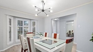 A dining area with a glass-top table, white chairs, and a modern chandelier. - 5BR 3.5BA Pool House – Comfortably Sleeps 15 (McKinney)