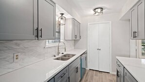 A modern kitchen with white cabinets, a double sink, and a built-in oven. - 5BR 3.5BA Pool House – Comfortably Sleeps 15 (McKinney)