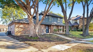 A two-story brick house with a front porch, large trees, and a well-maintained lawn. - 5BR 3.5BA Pool House – Comfortably Sleeps 15 (McKinney)