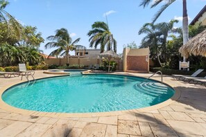 Piscina azul cristalina com espreguiçadeiras e palmeiras.