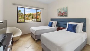 Habitación de hotel con dos camas, un escritorio, una silla y un ventanal con vistas a palmeras y edificios.