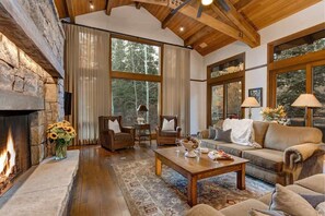 A cozy living room with a stone fireplace, large windows, and comfortable seating.
