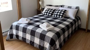 Un letto rifatto con cura, una coperta a quadri, una testiera in legno e una lampada da comodino.