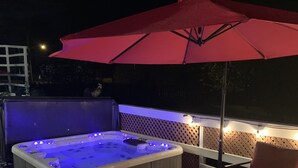 Una vasca idromassaggio con un ombrello rosso e luci, circondata da un pavimento in legno e una sedia.