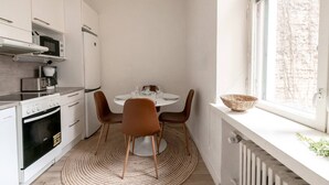 Et kompakt køkken med moderne hårde hvidevarer, et spisebord med stole og udsigt gennem et vindue.