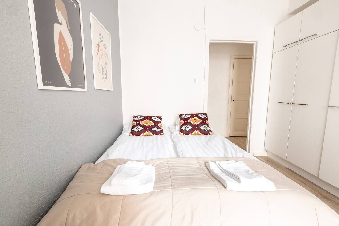 A hotel room with a bed, two pillows, a wardrobe, and a door.
