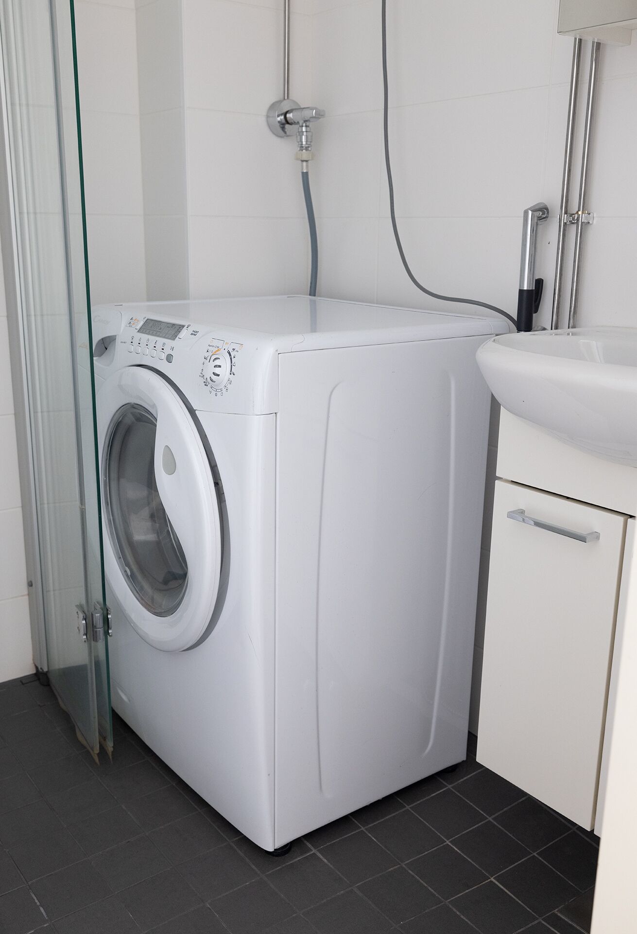 A compact, modern laundry room with a front-loading washing machine, a small sink, and a glass door.