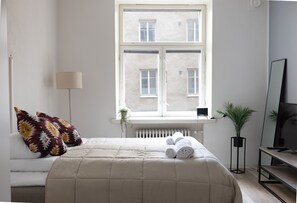 Une chambre avec un lit, une fenêtre, un radiateur, une plante et un téléviseur.