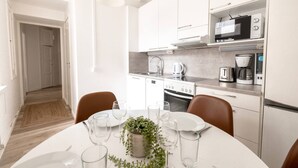 Et moderne køkken med hvide skabe, en mikrobølgeovn, en kaffemaskine og et spiseområde med et bord dækket til to personer.