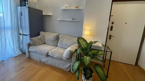 Ein gemütlicher Wohnraum mit einer Couch, einem Blumentopf, einem Kühlschrank und einer Tür.