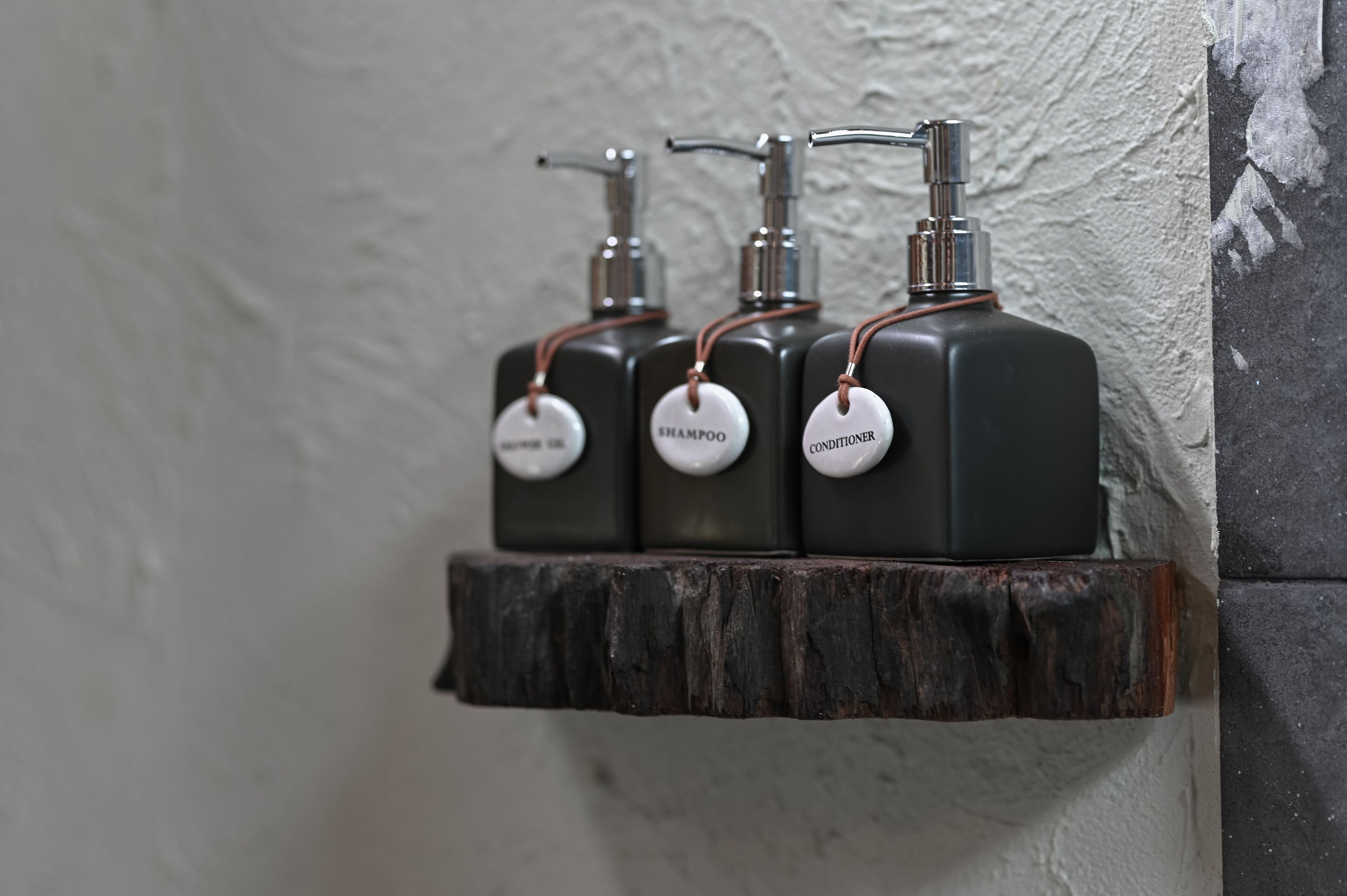 Three black bottles with copper tubing on a rustic wooden shelf against a textured wall.