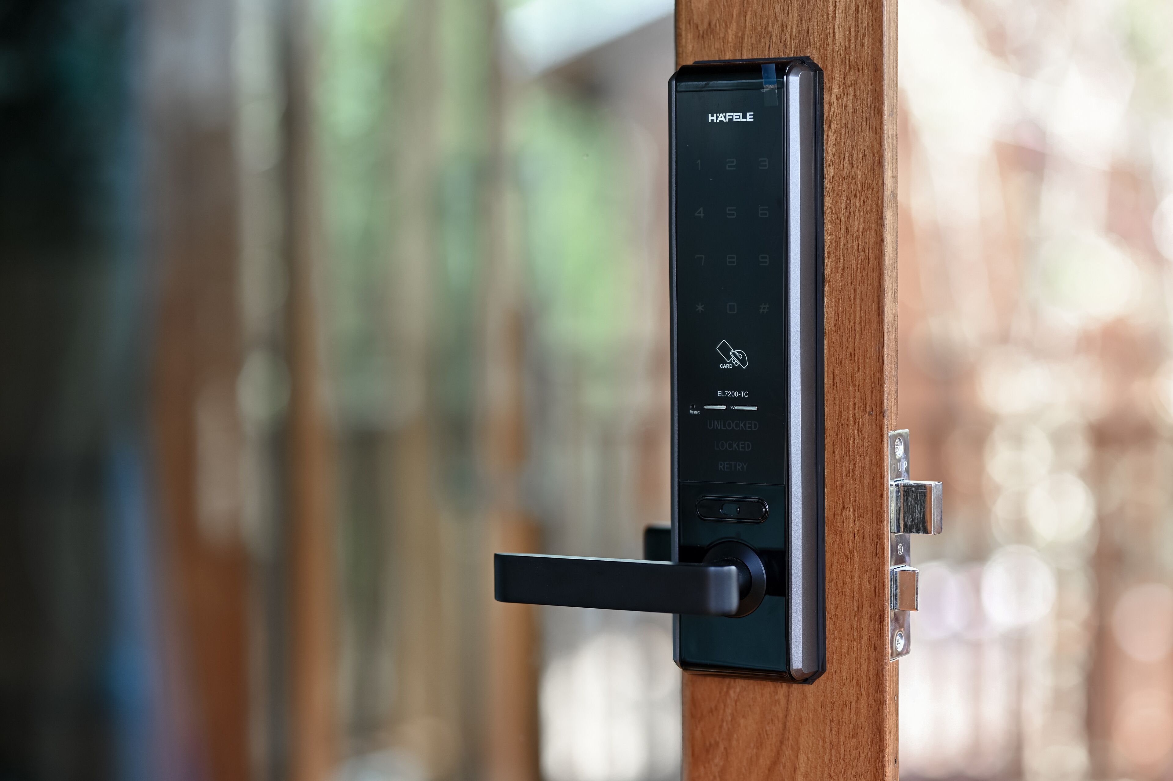 A modern electronic door lock with a keypad and a card reader, attached to a wooden door.