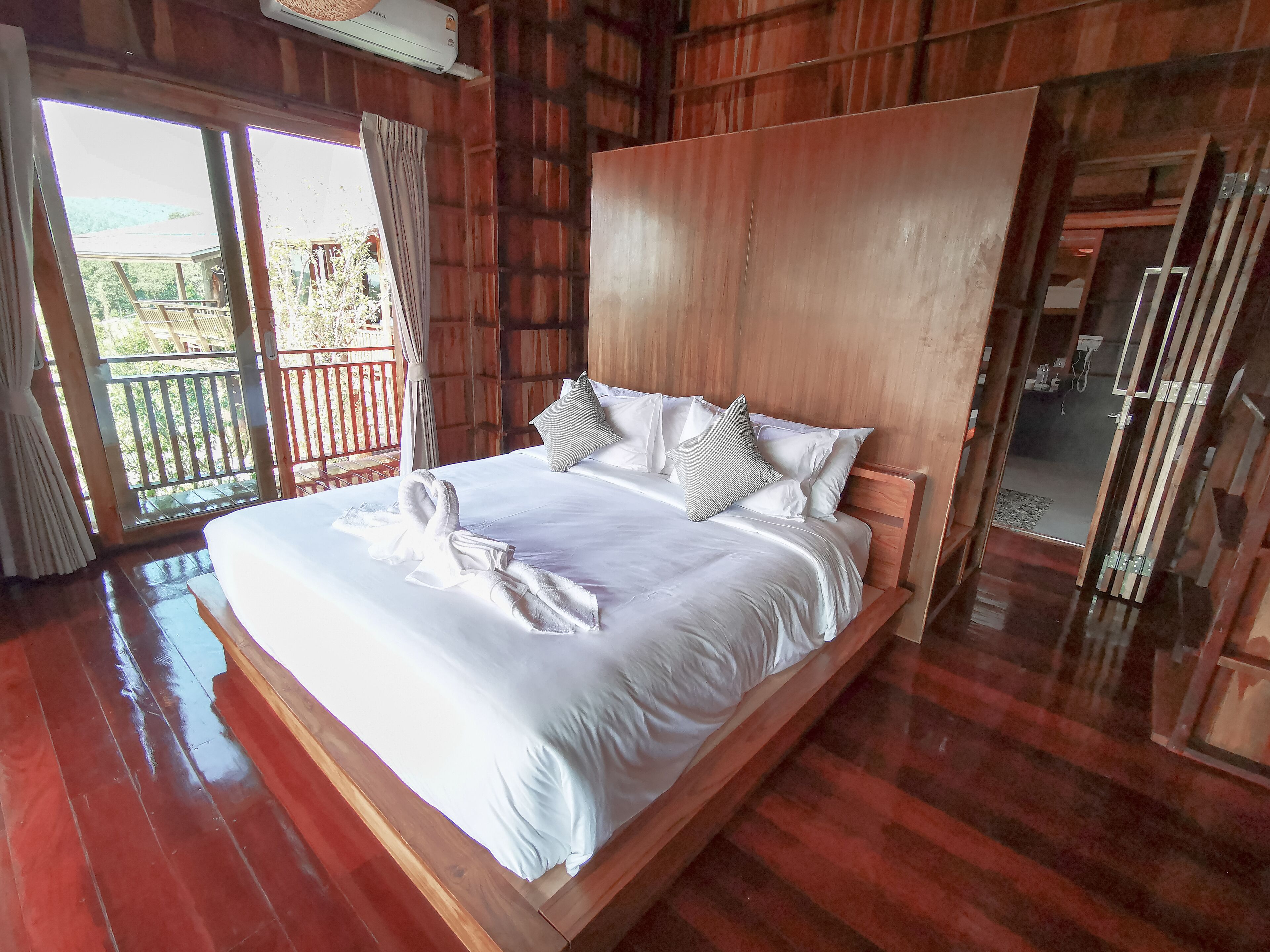 A spacious bedroom with a large bed, wooden headboard, and a balcony with a view.