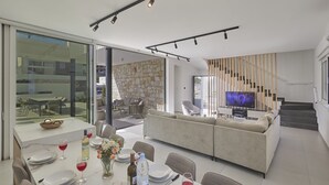 Un espacio habitable moderno con comedor, sofá, televisor y escalera.