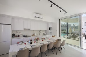 Une cuisine moderne avec des meubles blancs, un coin repas avec une table dressée pour six personnes, et une vue sur une piscine à l’extérieur.