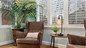 Een knus ingerichte kamer met een bruine fauteuil, een bijzettafeltje met een lamp en een grote potplant.